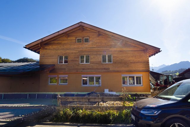Holzfassade eines Hauses, Erdgeschoss mit gelber Dämmung, Bagger auf Baustelle