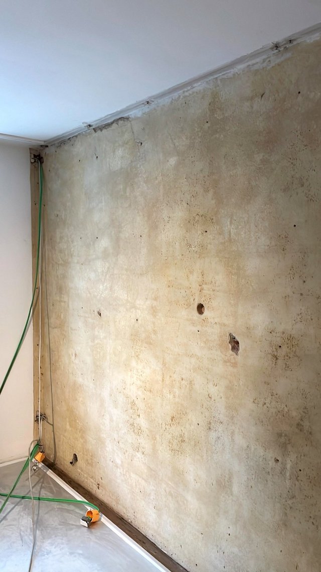 Fleckige Wandfläche mit Bohrlöchern und einer Ausbruchstelle, Boden mit Folie abgedeckt