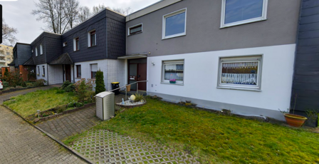 Reihenhausfassade mit Fenstern, Eingang, Vorgartenrasen und Gehweg.