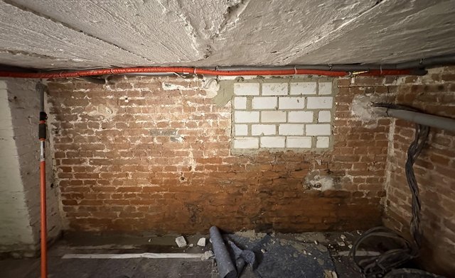 Ziegelwand im Keller mit ausgebesserter Öffnung und Leitungen an der Decke