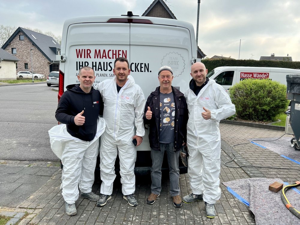 Drei ISOTEC Mitarbeiter und Kunde stehen vor Firmenfahrzeug auf Einfahrt.