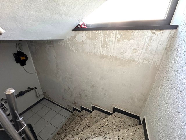 Abgeplatzter Wandbelag mit Verfärbungen und Laufspuren im Treppenhaus unter Fenster.