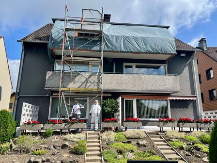 Geruest an Hausfassade, Balkon mit Folie abgedeckt, zwei Arbeiter davor