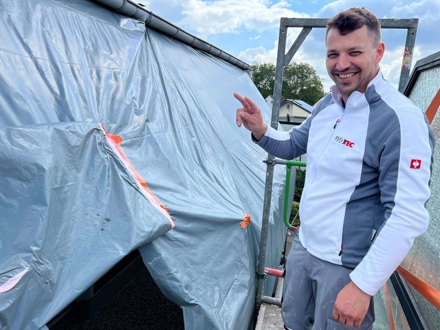 ISOTEC Mitarbeiter zeigt auf mit Folie abgedeckte Dachflaeche am Geruest