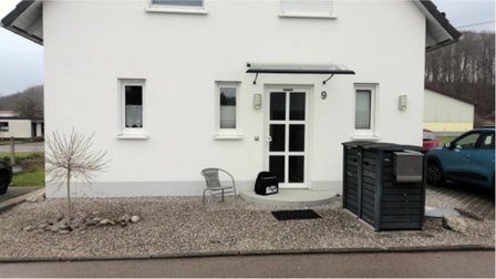 Eingangsbereich mit weißer Fassade, Kiesfläche und kleinem Baum