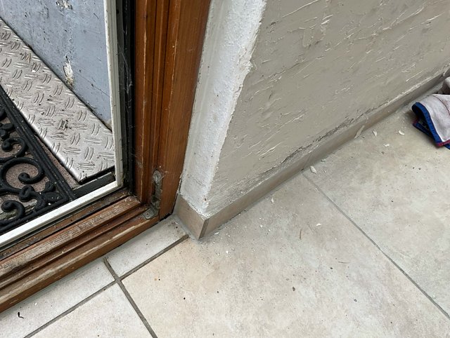 Abgeplatzter Wandputz am Sockel neben Holzrahmen und Fliesenboden.