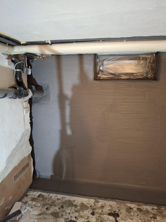 Kellerwand mit grauer Beschichtung, Rohrleitung und abgeklebtem Wanddurchbruch