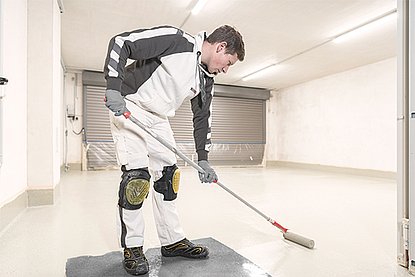 ISOTEC Mitarbeiter verteilt helle Masse auf Boden mit Farbrolle