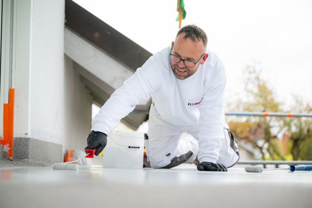 ISOTEC Mitarbeiter trägt helle Flüssigkeit mit Rolle auf Balkonboden auf.