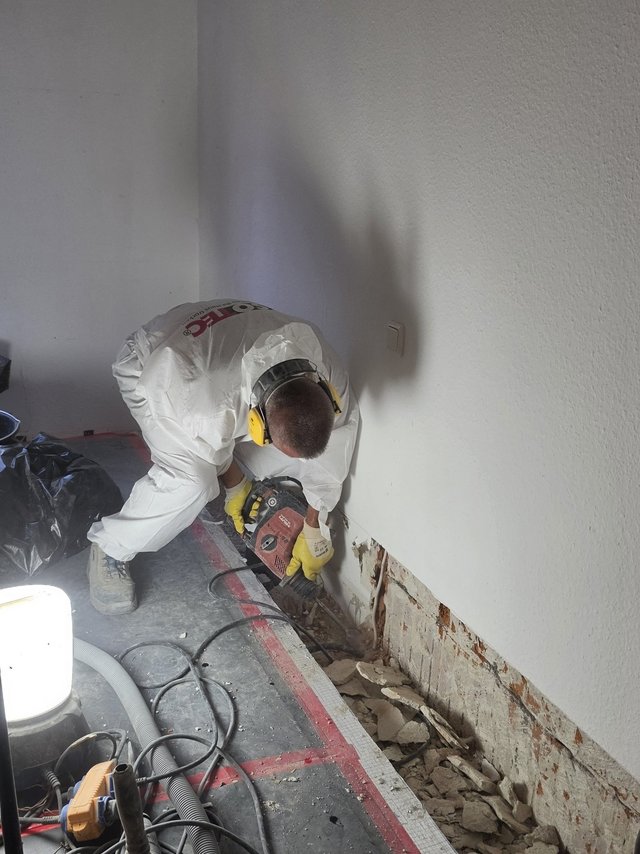 ISOTEC Mitarbeiter stemmt Wandputz im unteren Bereich einer Zimmerwand ab