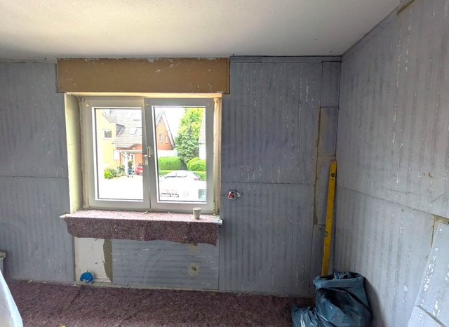 Fenster in grauer Baustelle, sichtbare Beschichtungsstreifen und gelbe Wasserwaage an der Ecke