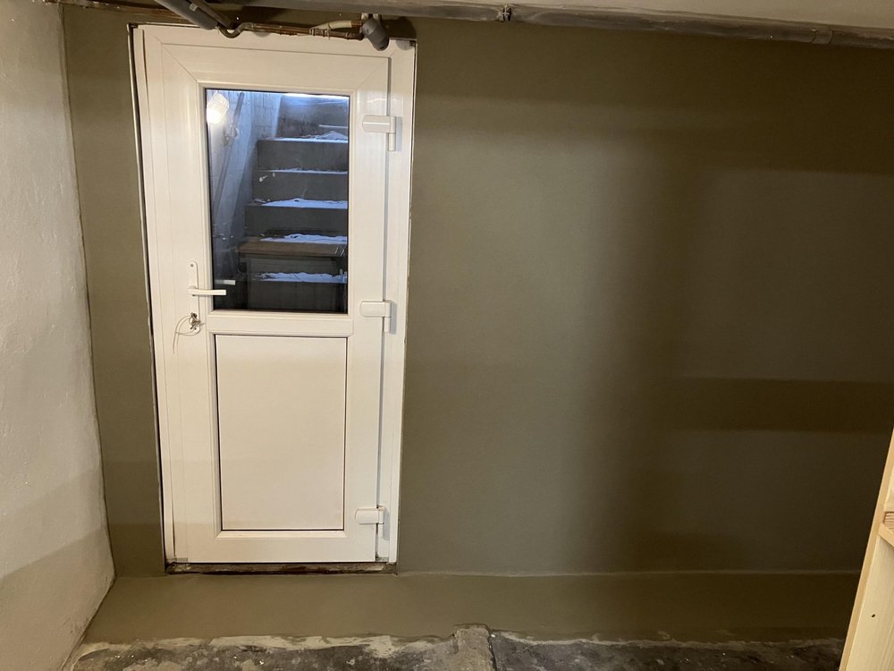 Weiße Kellertuer vor grauer Wand, Treppenaufgang hinter Glaseinsatz sichtbar