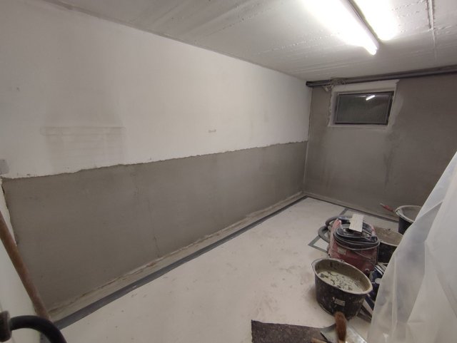 Kellerraum mit teils grauer Masse beschichteter Wand und Werkzeug am Boden