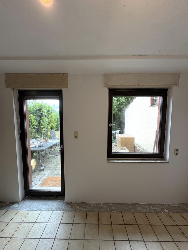 Weiß verputzte Zimmerwand mit Terrassentür und Fenster, Blick auf Pflasterterrasse.