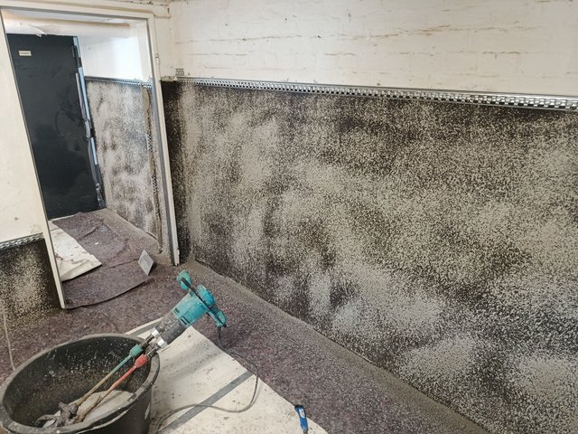 Schwarze Masse auf Kellerwand, Metallprofil montiert, Bohrmaschine und Mischeimer im Raum