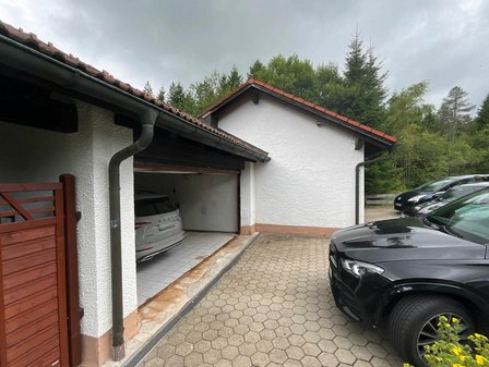 Offene Garage mit weiß verputzter Fassade, Autozufahrt und parkenden Fahrzeugen