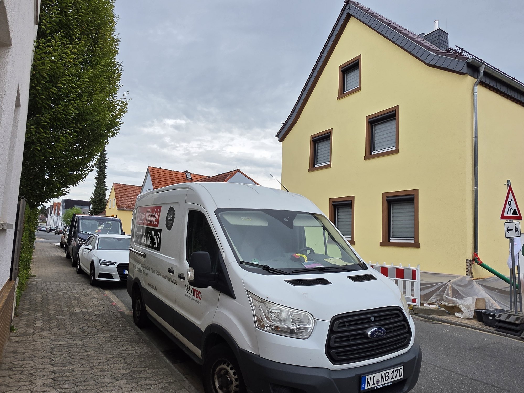 ISOTEC Transporter vor gelbem Wohnhaus mit Baustellenabsperrung in Wohnstraße