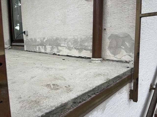 Riss und graue Ausbesserungsstelle am Sockelbereich neben Fallrohr auf Betonplatte