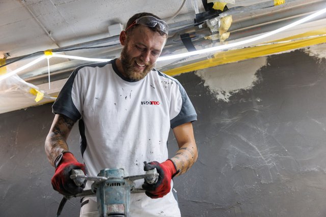 ISOTEC Mitarbeiter hält Bohrmaschine in Baustellenraum mit grauer Wandfläche