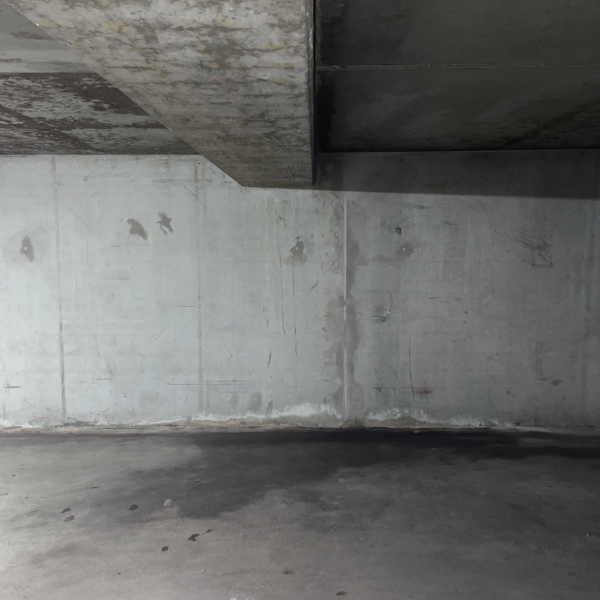 Betonboden mit dunklen Feuchteflecken vor grauer Kellerwand und Decke