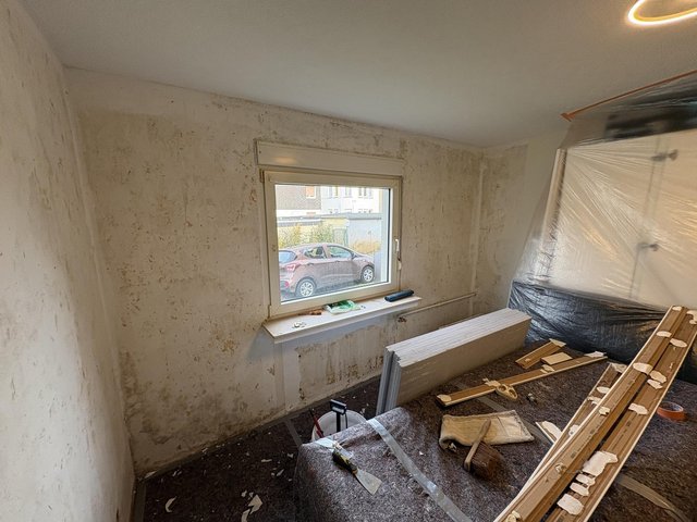 Renovierungsraum mit fleckigen Wänden, Fenster und abgedeckten Möbeln, Werkzeuge im Vordergrund