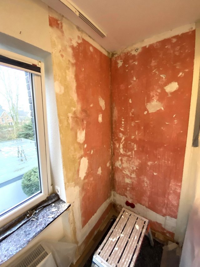 Abgeschabte rote und helle Wandflächen in Raumecke, Fenster und Klapptritt daneben