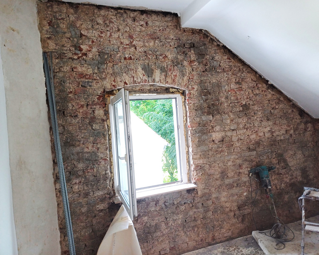 Freigelegte Ziegelwand mit offenem Fenster und Bauwerkzeug im Raum