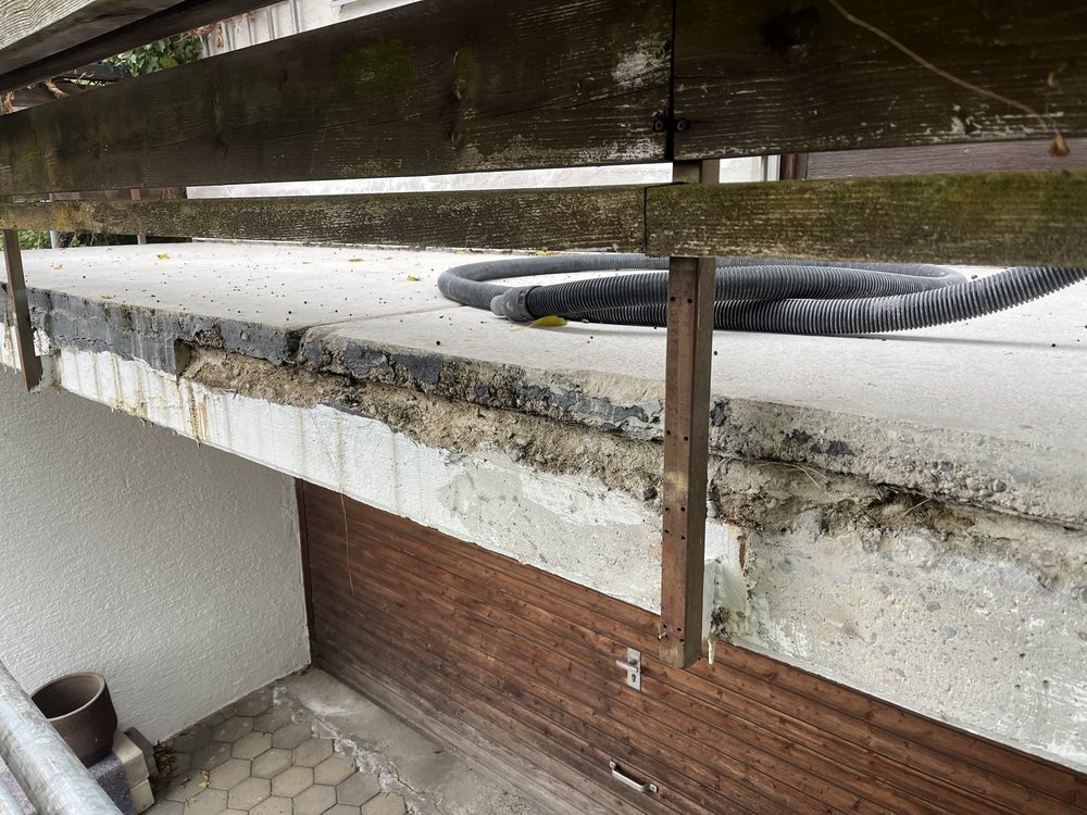 Beschädigte Betonkante am Balkon, schwarze Schlauchleitung auf Betonplatte.
