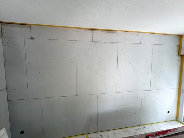 Helle Plattenwand mit Fugen, gelbe Abklebung an Kanten und Boden