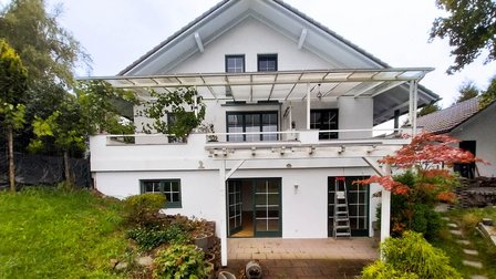 Weiße Hausfassade mit Terrassenüberdachung, Leiter vor Glastür und Garten