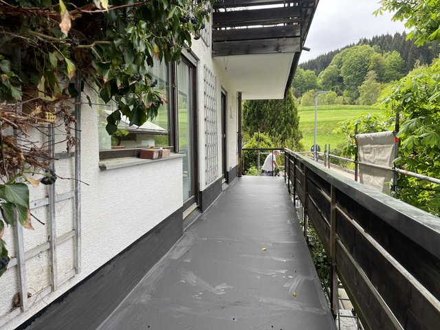 Mitarbeiter trägt graue Masse auf Balkonboden auf, Geruest am Gelander.
