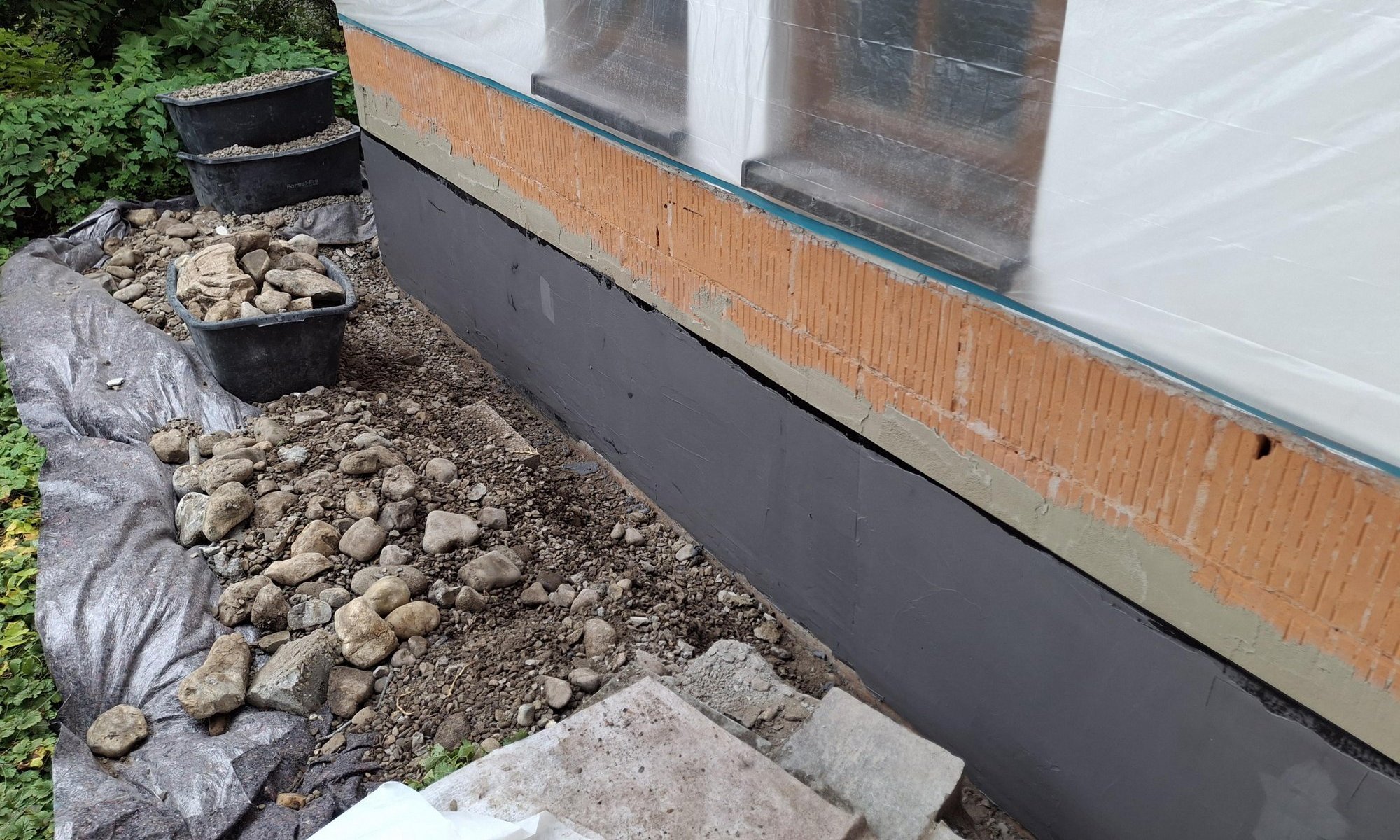 Schwarze Masse am freigelegten Gebäudesockel, Fenster mit Folie abgedeckt