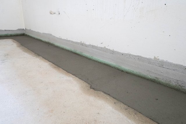 Graue Masse als Bodenkehle entlang Wand, grüne Dichtbahn am Übergang.