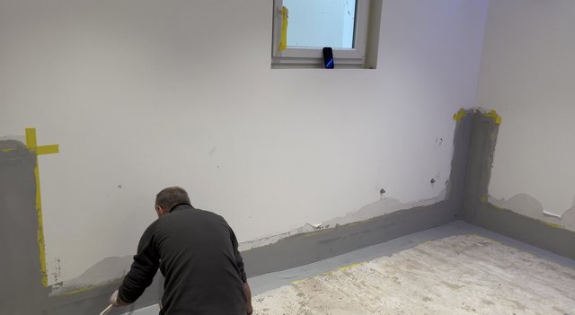 Arbeiter trägt graue Masse am Wand-Boden-Anschluss in einem Zimmer auf.