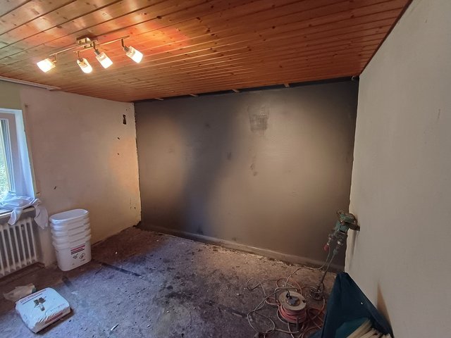 Zimmer mit grauer Wandbeschichtung, Holzdecke und freigelegtem Boden