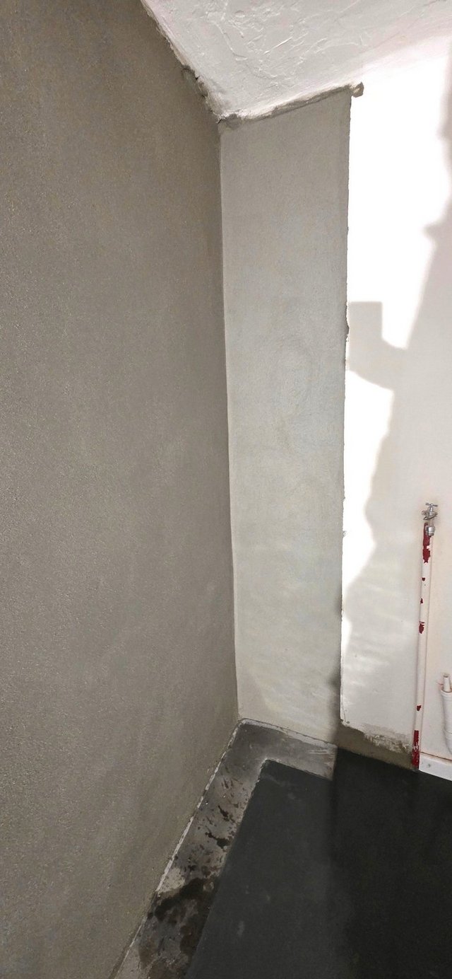 Graue Wandbeschichtung in Zimmerecke, schwarzer Bodenbelag