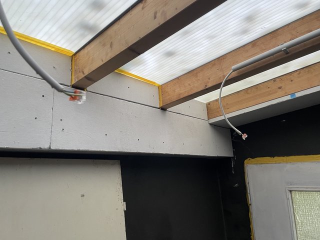 Holzbalken unter Stegplatten, graue Masse an der Wand, Kabel mit Verbindungsklemmen hängen herab