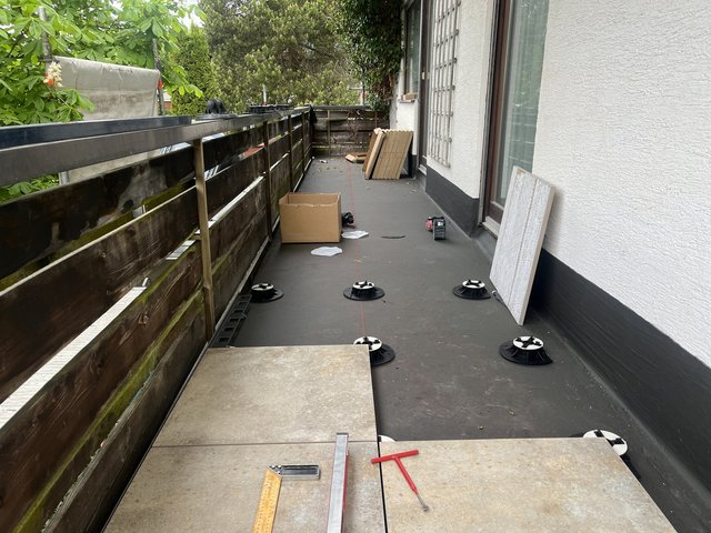 Balkon mit Stelzlagern, Fliesenplatten und Messwerkzeug für Terrassenbelag