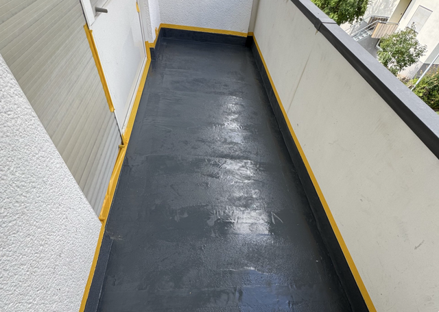 Schwarze Masse auf Balkonboden, Ränder mit Klebeband abgeklebt