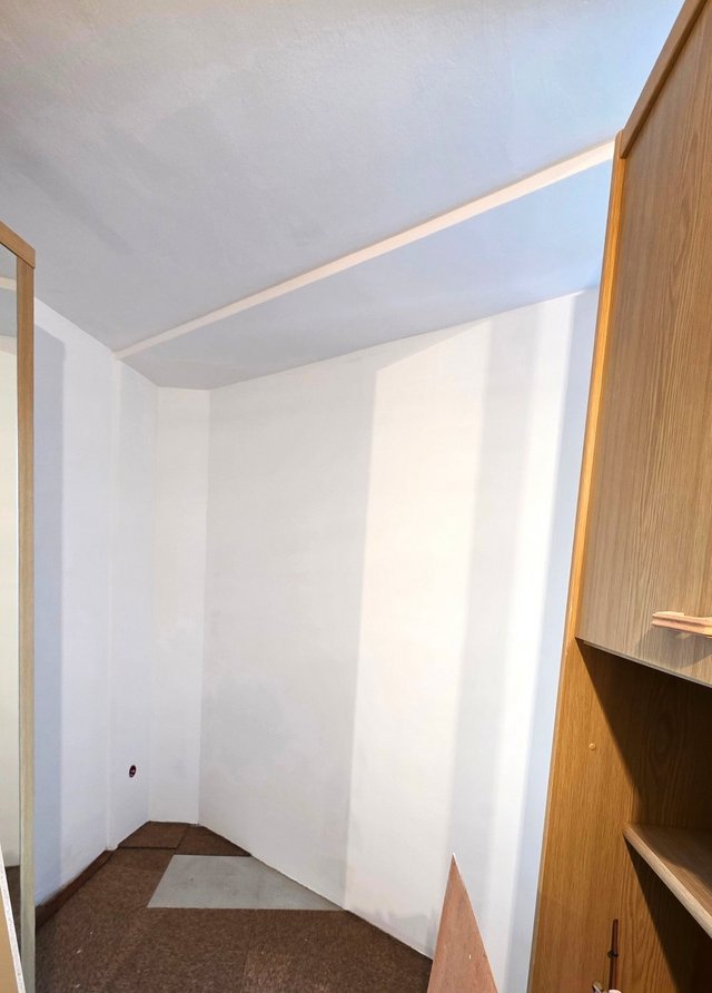 Weiß gestrichene Nische mit Dachschräge und Holzschrank