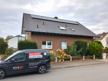Ziegelhaus mit Solarpanelen und ISOTEC Fahrzeug am Straßenrand