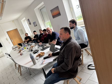 Mehrere Männer sitzen an einem Konferenztisch im hellen Besprechungsraum.