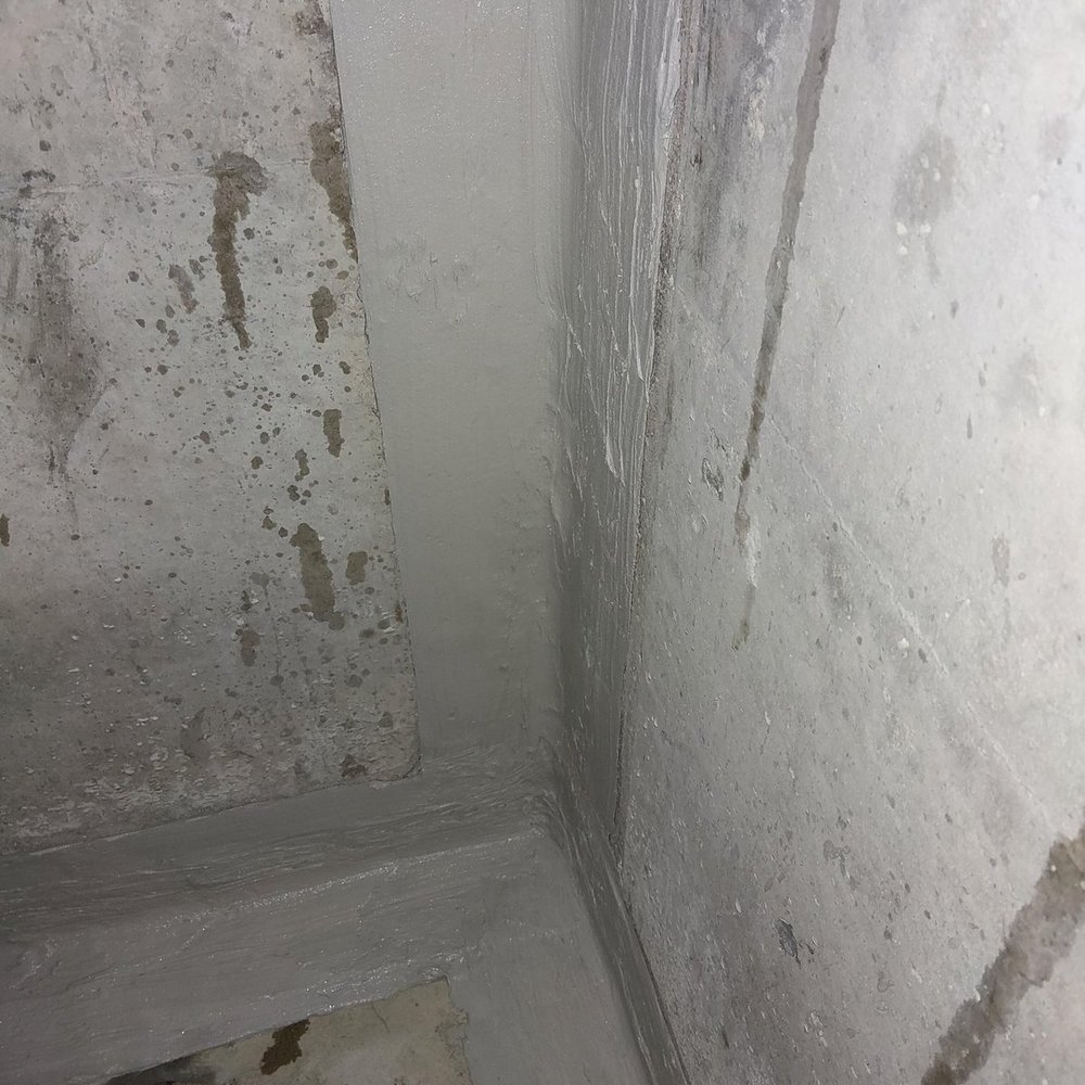 Graue Masse in Wand-Boden-Ecke eines Kellerraums aufgetragen