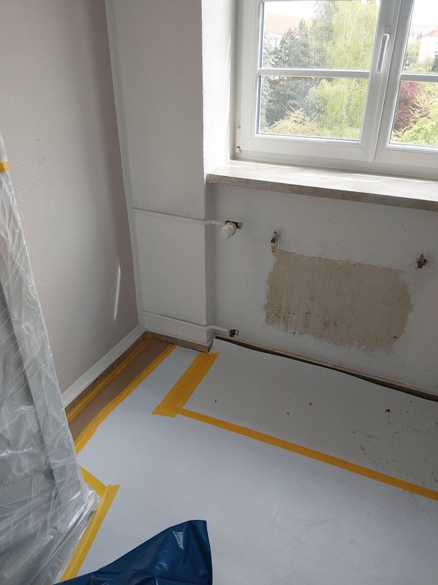 Abgedeckter Boden mit Klebeband, freigelegte Stelle an Wand unter Fenster.