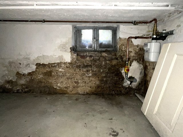 Beschädigte Kellerwand mit freiliegendem Mauerwerk unter kleinem Fenster