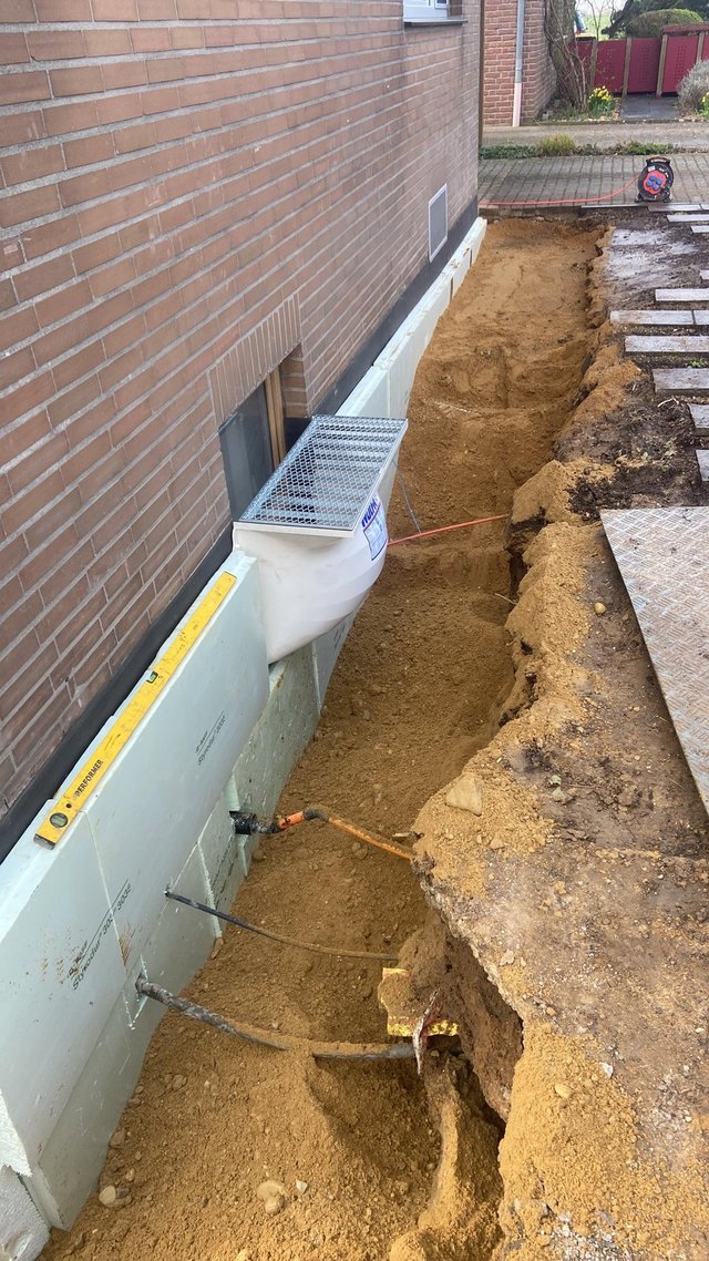 Freigelegte Kellerwand mit heller Dämmplatte und Drainagegraben am Gebäude