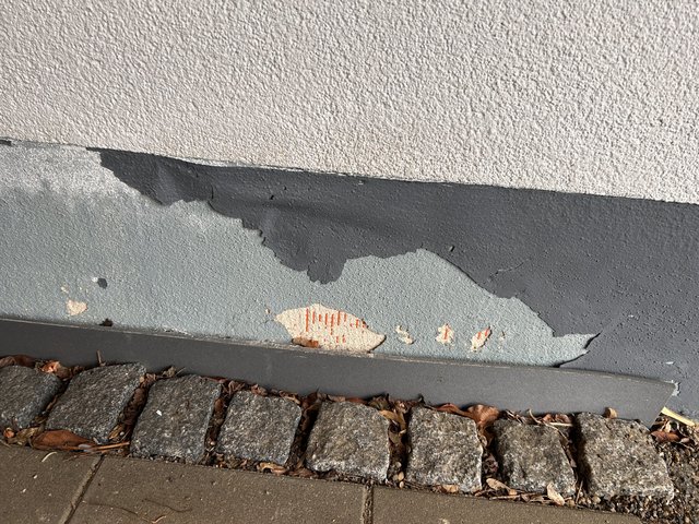 Abblätternde schwarze Beschichtung an Gebäudesockel über grauer Dämmplatte