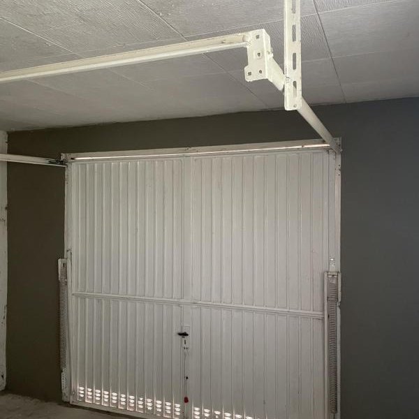Weißes Garagentor mit Führungsschiene in grauer Garage