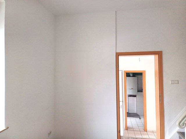 Helle Zimmerwand mit Blick durch Türrahmen in gefliesten Raum