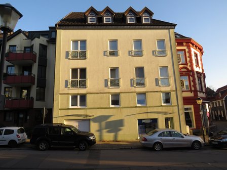 Mehrstöckiges Wohnhaus mit Balkonen und parkenden Autos in Straßenansicht.